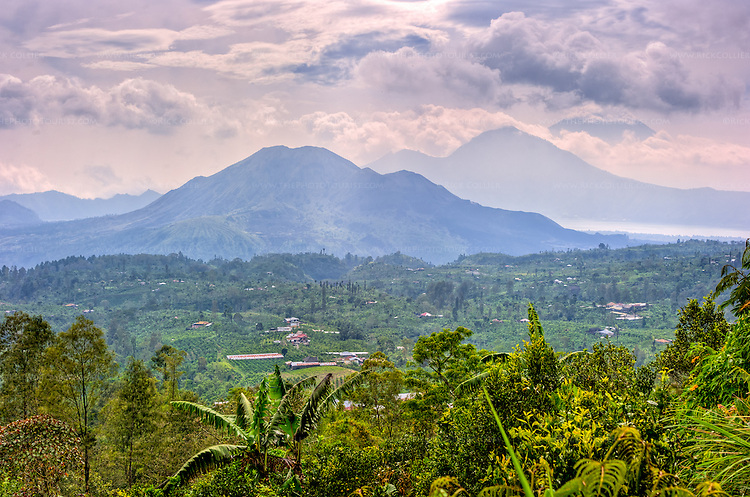 Bali's spectacular Mount Batur volcano and crater lake frame the view of countryside from the high road climbing the ridge line originally formed by the rim of the volcano's caldera, traveling from the north coast south to Ubud. Behind the "new" Mount Batur volcano lies the crater lake (Lake Batur). Bali's tallest mountain, Agung, frames the view in the background. (Bali, Indonesia; HDR image)