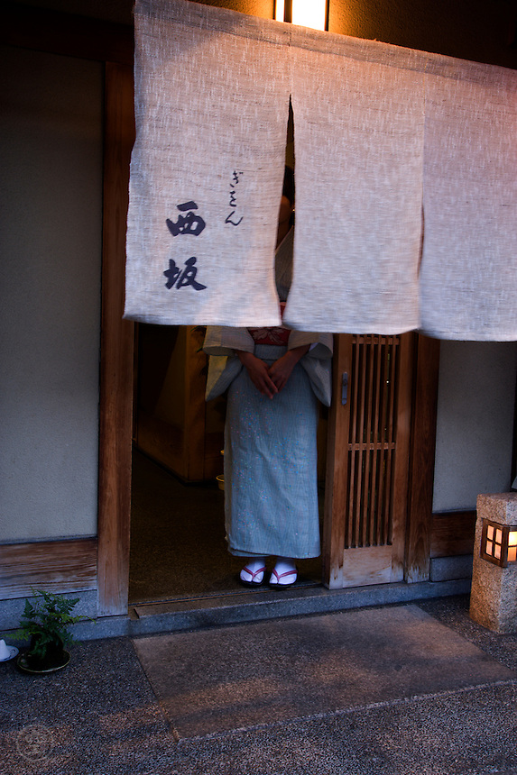 A kimono clad waitress waits at the doorway of a Gion restaurant to welcome guests, Kyoto.
