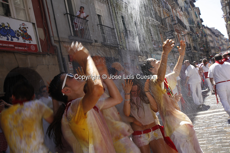 Some people throwing water over revelers which are enjoying of the first day of Sanfermines in city hall square, in Pamplona, northern of Spain. San Fermin starts with the launch of a rocket, which is known as "chupinazo". San Fermin festival is worldwide known because the daily running bulls.