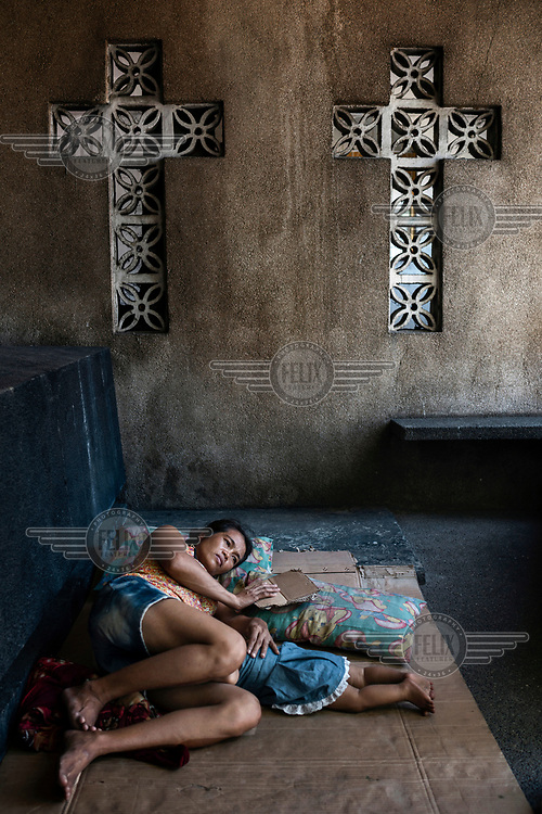 Noemi Canilang, 41, rests beside a tomb with her grandson John Lewis de la Cruz, eight months, in the Espiritu family mausoleum, in Manila North Cemetery, which she is paid to look after by the family and therefore is allowed to sleep in with five other members of her family. Manila North Cemetery is home to thousands of 'informal settlers' who have built shacks using in and around the mausoleums, crypts and tombs. In comparison to the city's dangerous shantytowns the cemetery is relatively quiet and safe. However, water must be collected from a few public wells and the electricity supply is erratic, usually stolen from mains cables. In the summer the sweltering heat drives people to sleep outside often on top of the tombs.<br />
<br />
Some of the residents live in the crypts and mausoleums of wealthy families, who pay them a stipend to clean and watch over them. Others make a living carving headstones or selling candles to visitors and helping out at funerals as the daily life of the cemetery goes on around the people who live there.
