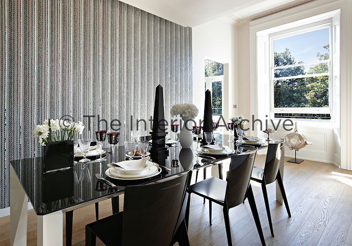 A fluted mirror mosaic feature wall is the unusual backdrop in a contemporary dining room. A polished black lacquer table is set for dinner.