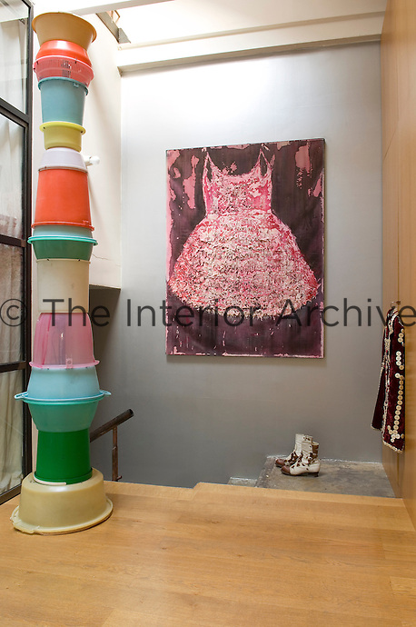 A tall column made out of plastic buckets, a large painting and a pair of boots form the focus of this landing
