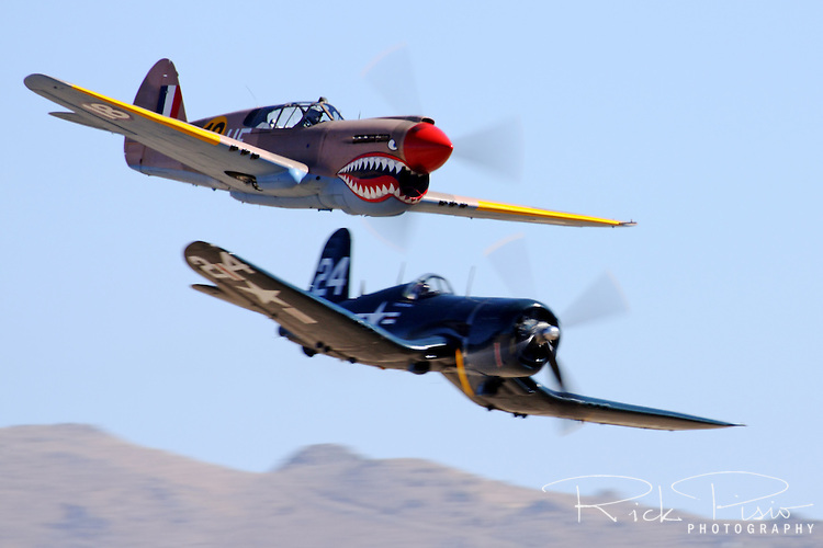 John Curtiss Paul in the P-40E Warhawk "Sneak Attack" passes "Race 24" piloted by Jimmy Leeward during the 2009 Unlimited Bronze Finals. Paul flew the Warhawk to a third place finish with a speed of 324 mph and Leeward flew the Corsair to a 4th place finish at a speed of 323 mph.