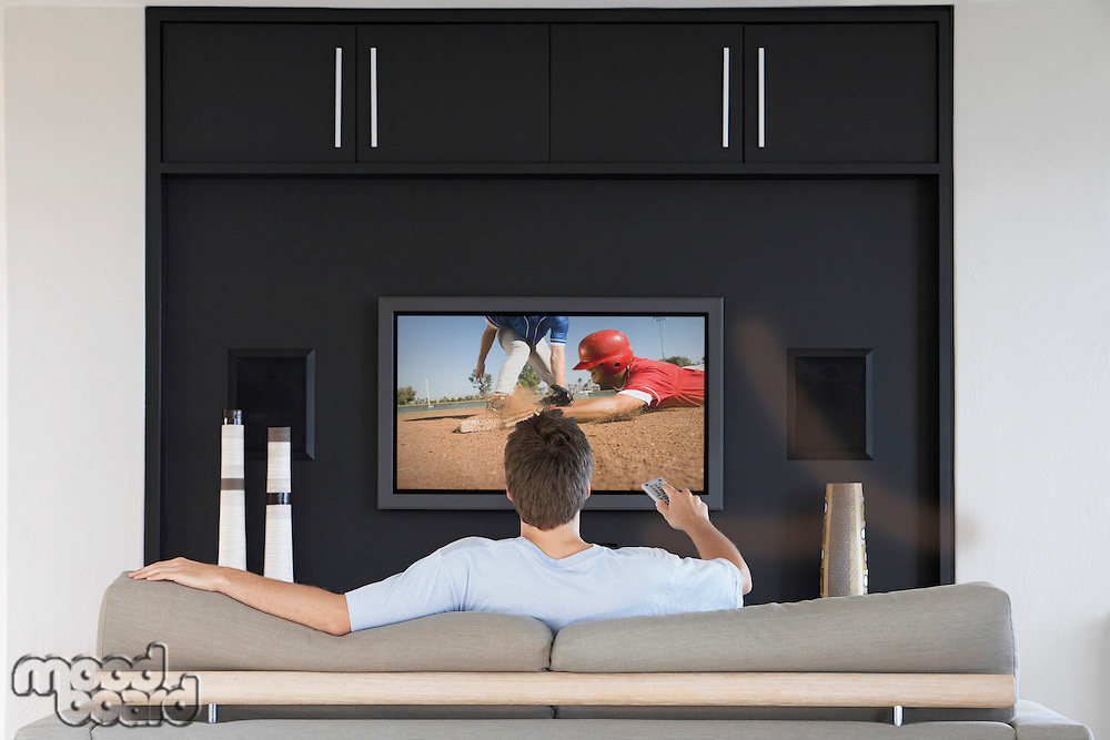 Back view of mid-adult man changing channels with television remote control in living room