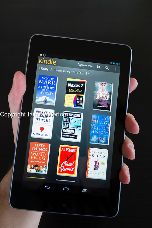 Man holding Google Nexus tablet computer running android operating system and browsing e-books in Kindle library