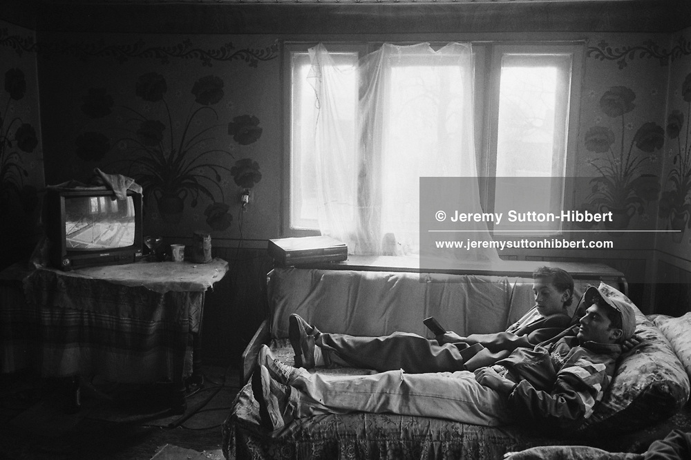 Bratu Mihai and Puia Chivu, wearing cap, watch television in a house in the Kalderash Roma camp of Sintesti, near Bucharest. Many of the young men of the camp do not have employment and make a living helping their families or with a variety of menial work.
