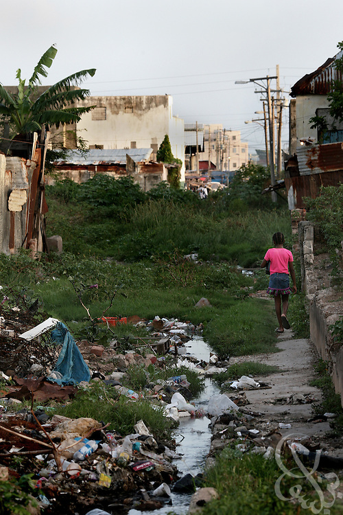 A Jamaican girl walks a trash strewn landscape past an open sewer June 17, 2008 in an inner-city ghetto area of Kingston, Jamaica. A recent United Nations report found that the great majority of victims of violent crime in Jamaica live in ghetto areas, and suffer disproportionately high rates of unemployment, limited clean water supplies and electricity.