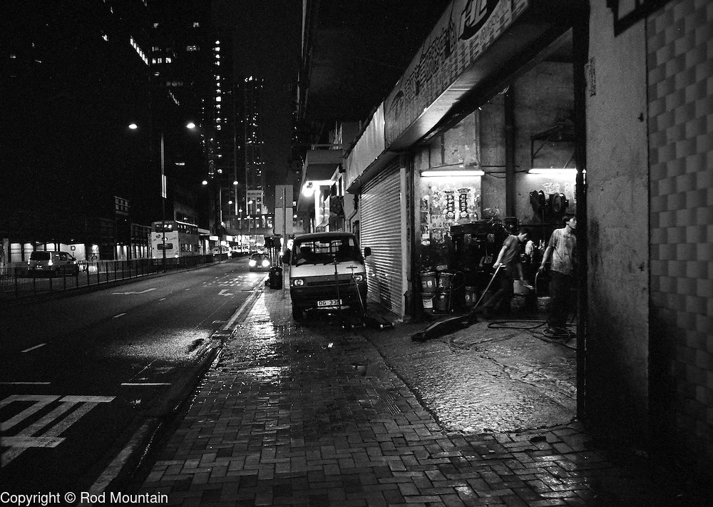 Two young men begin to put away their equipment as they close late into the evening at a local Hong Kong garage.