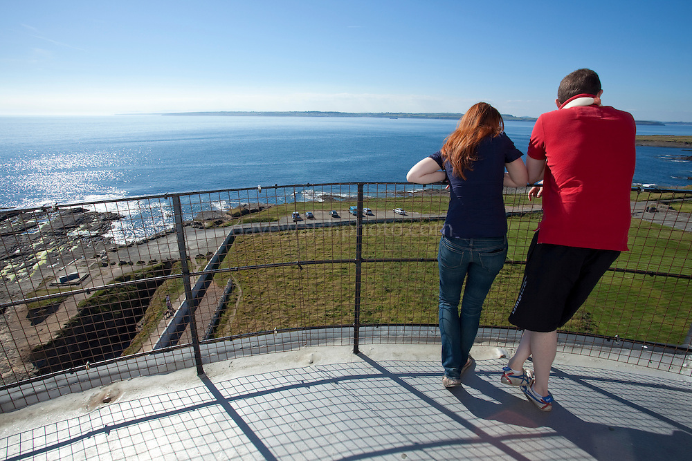 A young couple look out to sea from the Hook Lighthouse, Fethard on Sea, Wexford, Irelan, one of the oldest lighthouses in the world, which has been in use since the 12th or 13th century. Although a fire beacon was operated here to warn shipping as early as the 5th century, it was with the arrival of the Normans in that the tower was built. The existing lighthouse incorporates the original Norman fortress structure.