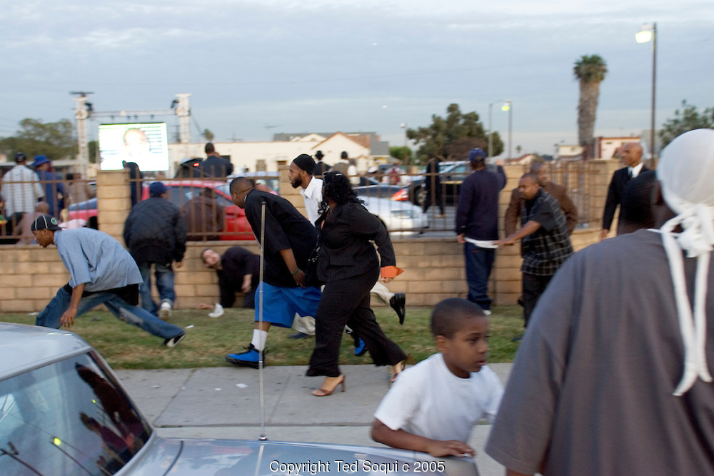 People take cover as gangbangers shoot bullets into the air at the Funeral services for Stanley "Tookie" Williams at Bethel A.M.E. Church in S. Central LA. About 2000 people attended the services which included many gang members. The funeral was a star studded event attended by Jesse Jackson and rapper-actor Snoop Dogg, Nation of Islam leader Louis Farrakhan, and Bianca Jagger. Loudspeakers and a large TV screen brought the service to many of the onlookers who could not get inside the packed church..