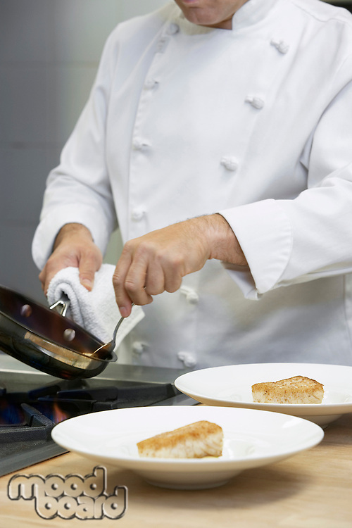Male chef holding frying pan serving food onto dishes in kitchen