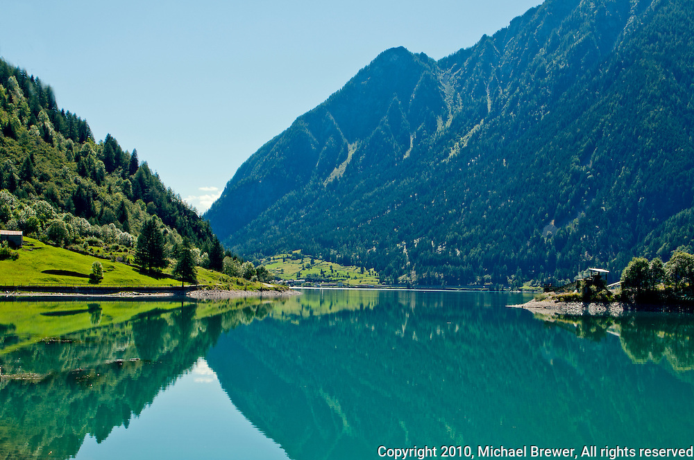 Reflection of the Swiss Alps in the beautiful blue lake at Le Prese in Graubunden, Switzerland.