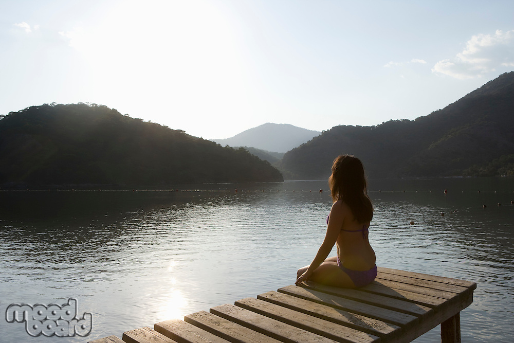 Young woman sits on lakeside jetty at dawn