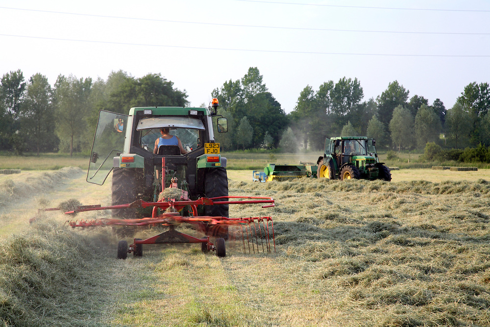 Farm worker raking hay into rows with tractor with baler