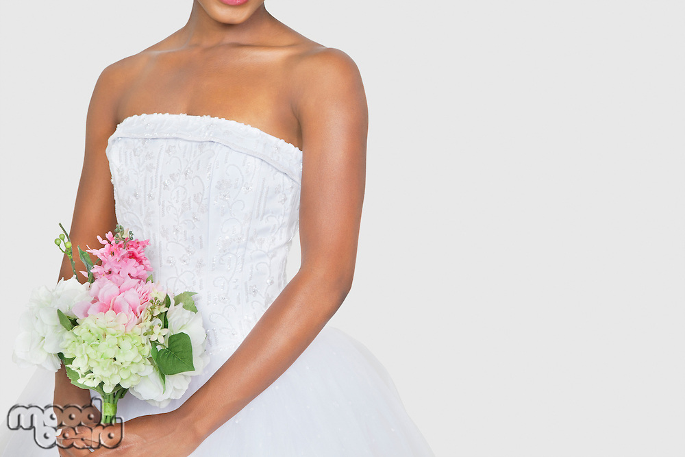 Midsection of bride holding bouquet over gray background