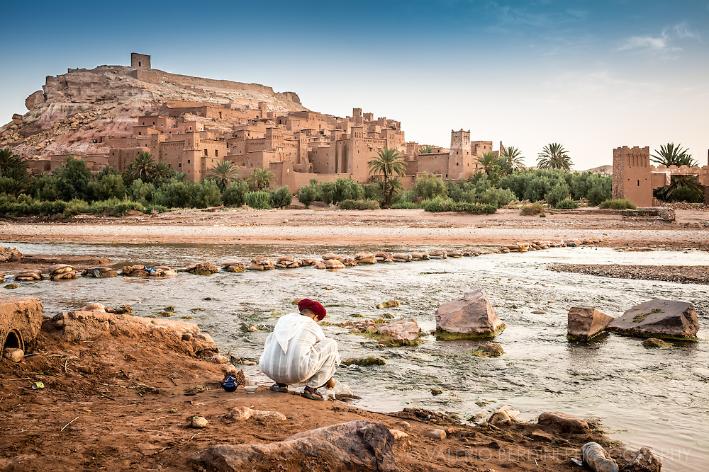 A man in early morning washes up teapots on the bank of the river flowing next to Aït Benhaddou old city (Ksar). This city, sited in Morocco, on the road from Marrakech to Sahara, has become famous for having staged several Hollywood blockbuster movies including the Gladiator and the Passion of Christ, and is protected by UNESCO as a world heritage site.