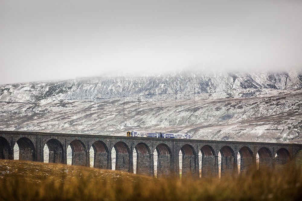 © Licensed to London News Pictures. 23/11/2015. Ribblehead UK. A train travels across the Ribblehead Viaduct in the shadow of the snow covered Whernside mountain as temperatures are expected to warm up today after a freezing weekend. Photo credit: Andrew McCaren/LNP