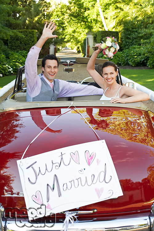 Mid adult bride and groom in retro car waving hands