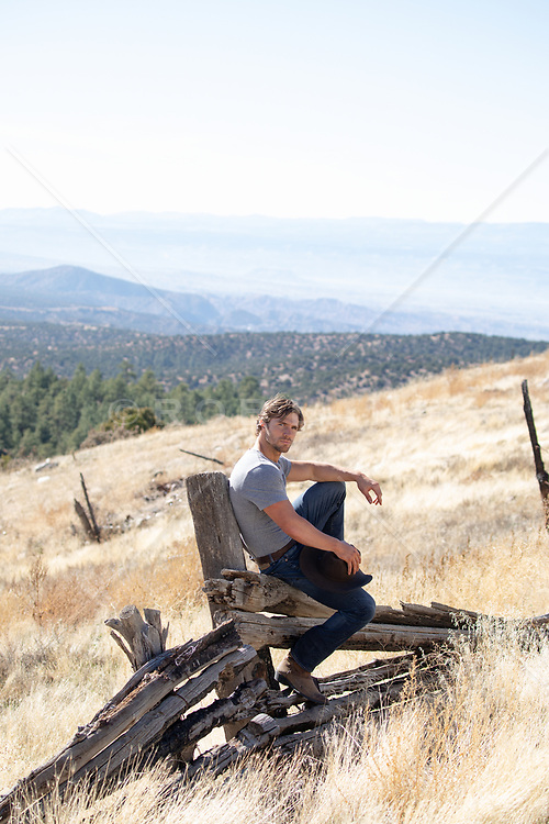 cowboy by a rustic fence on a mountain top