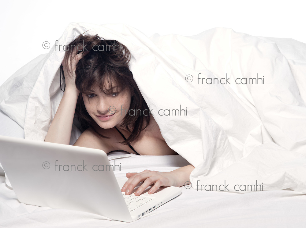 young woman in a white sheet bed on white background with a pc computer laptop