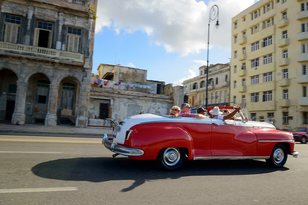Tourists ride in the back of a red vintage car on the Malecon, the seaside promenade in Havana, Cuba.